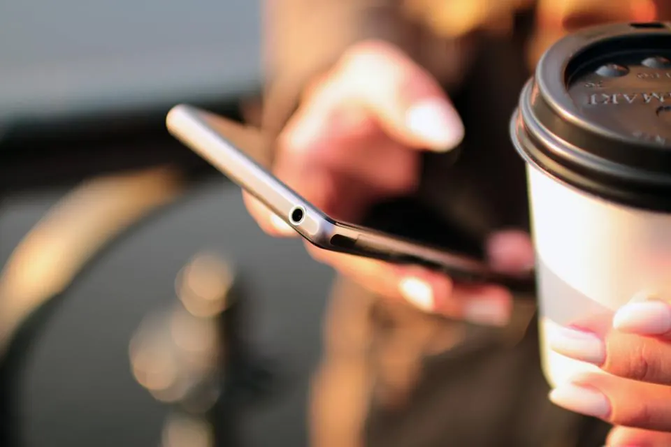 Telemóvel na mão ao lado de um copo de café, num café ao fim do dia